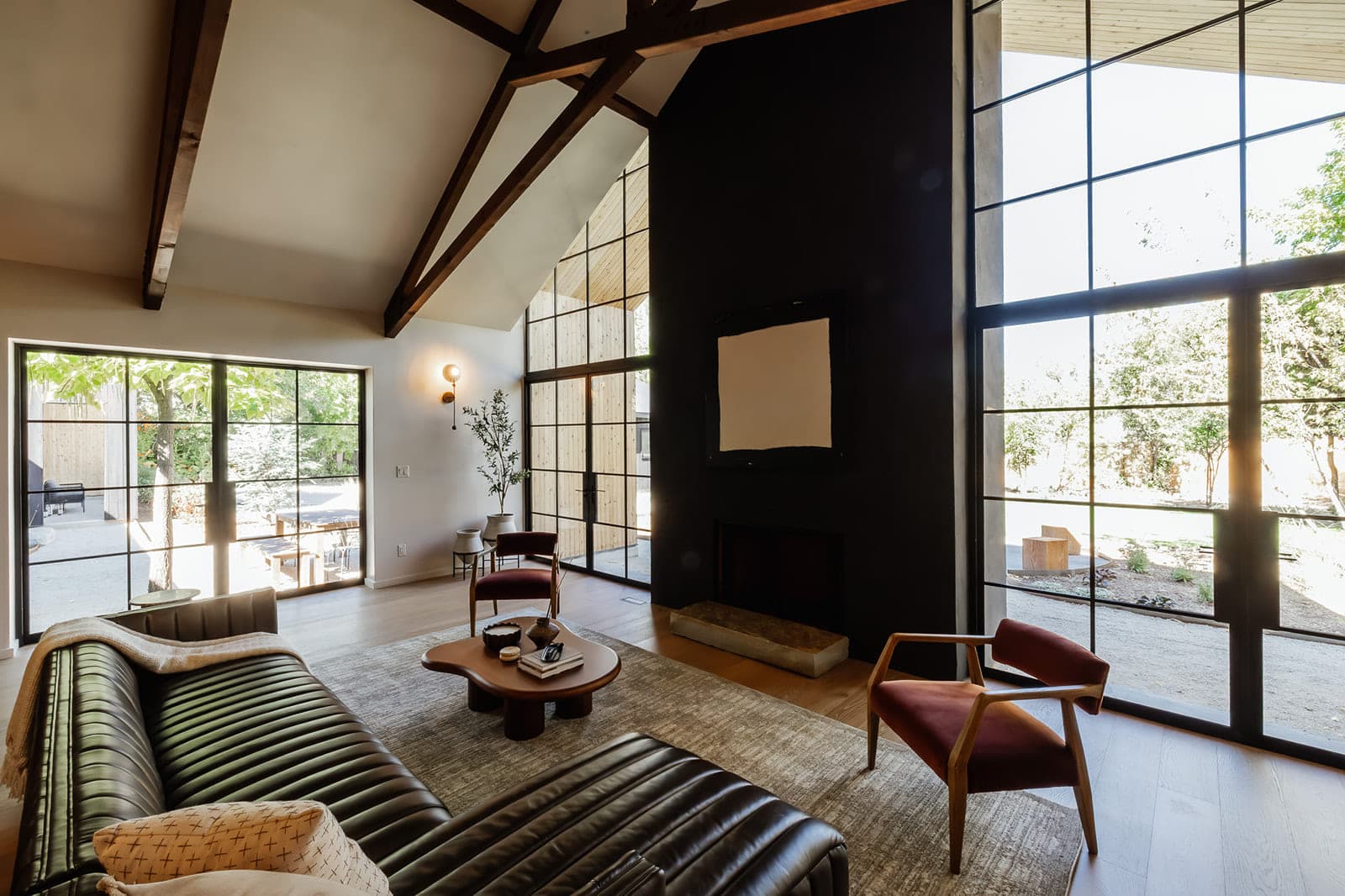 Showcase home great room under exposed timber trusses, with steel glazing on both sides.