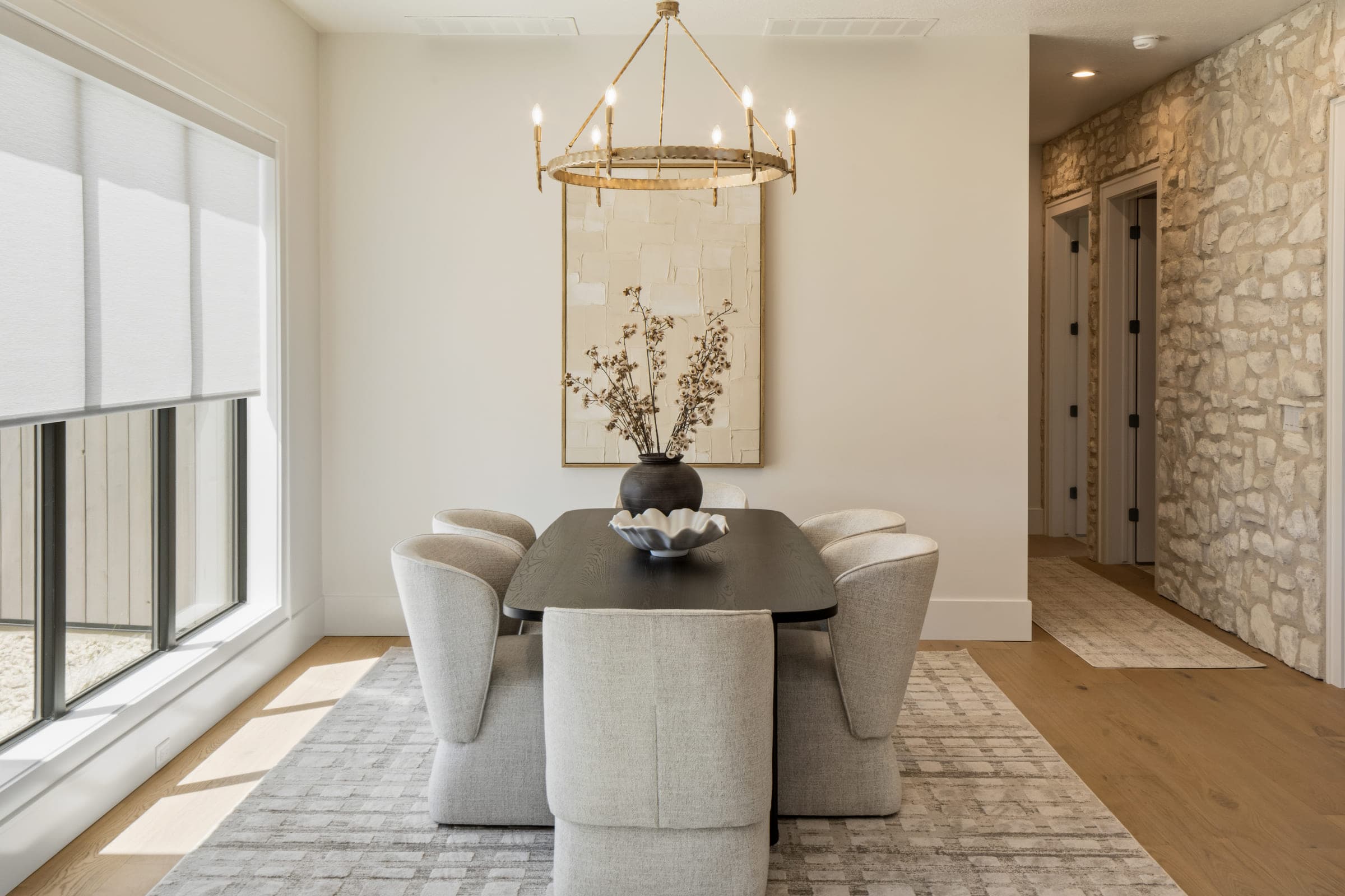 Model home dining room lit by a brass ring chandelier against a stone accent wall.